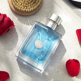 Versace Pour Homme Eau de Toilette 100ml bottle lying on a light surface with rose petals and grooming brush, highlighting its fresh masculine appeal.