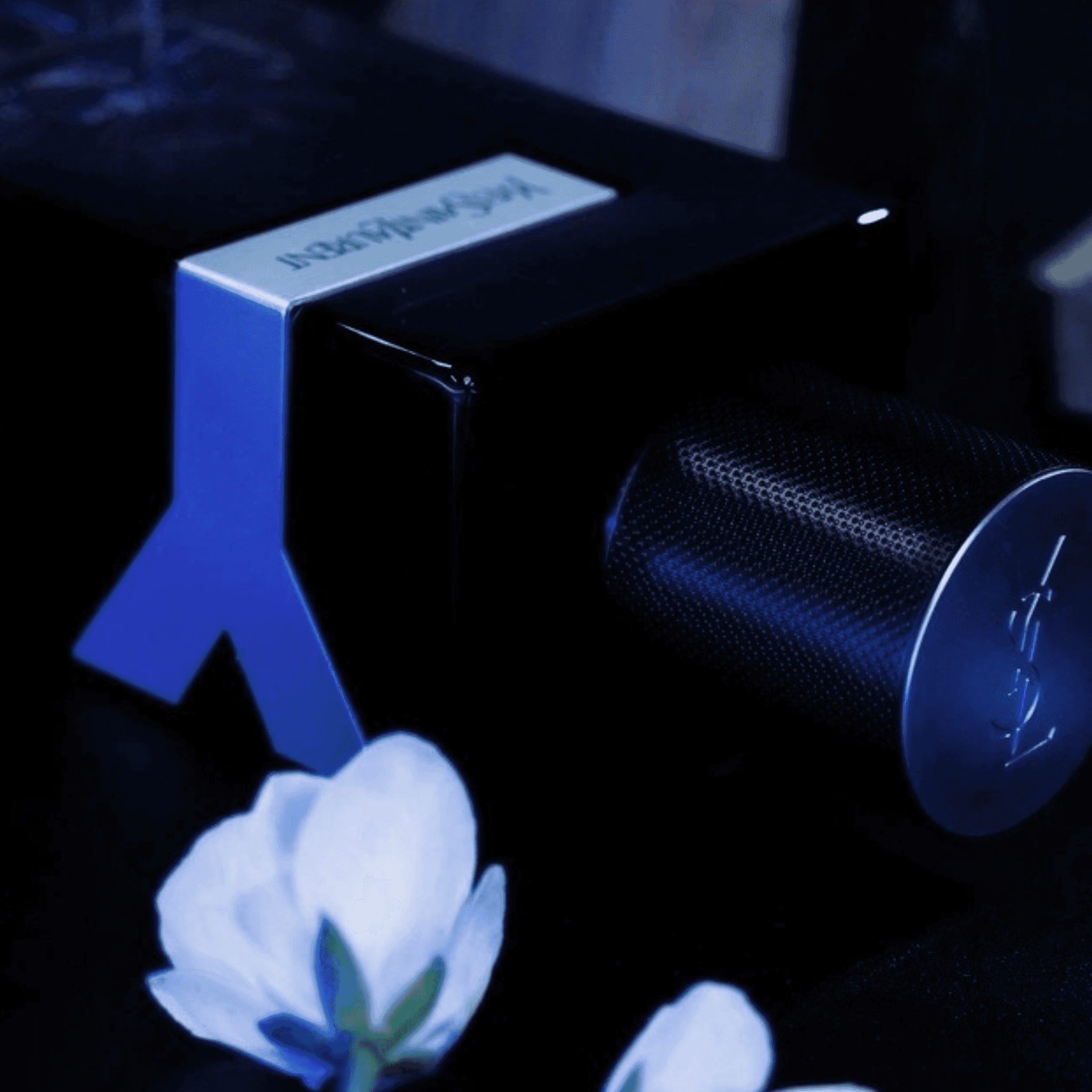 Close-up of YSL Y Eau de Parfum bottle lying on its side with Y-shaped detail and floral accent, highlighting premium design.